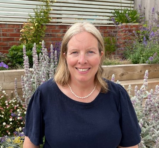 Profile photo of Rosie in a garden with colourful summer flowering plants behind her